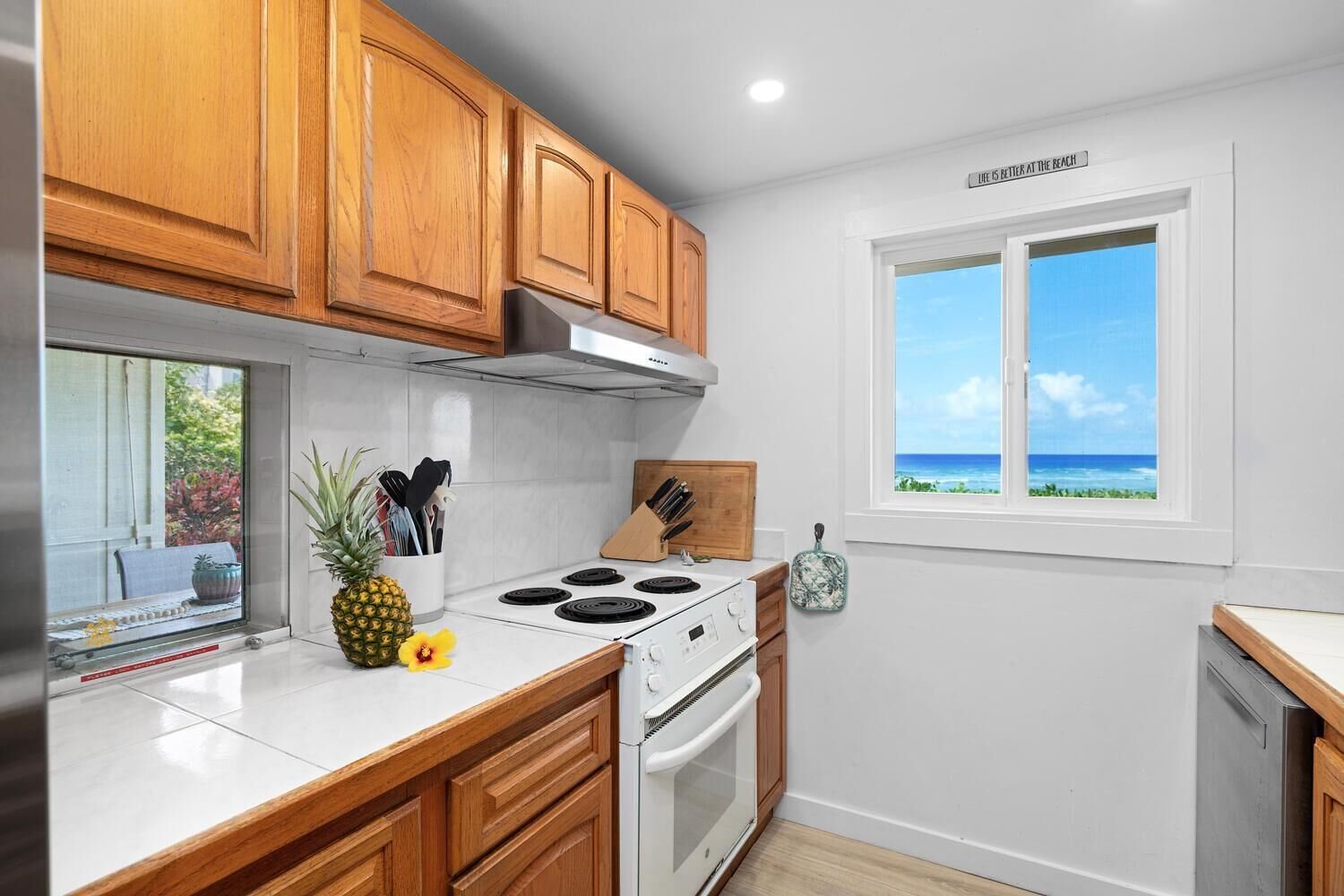 A kitchen with wooden cabinets, a white stove, and a window with a view of the ocean.