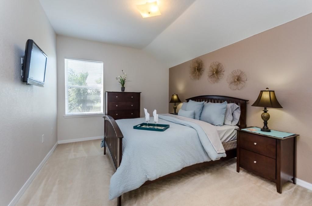 A bedroom with a bed, bedside tables, a TV mounted on the wall, a window, and a ceiling light.