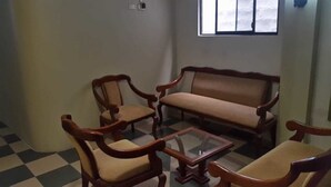 A room with a checkered floor, a wooden sofa, two wooden chairs, and a glass coffee table. - Unihotel (Loja)