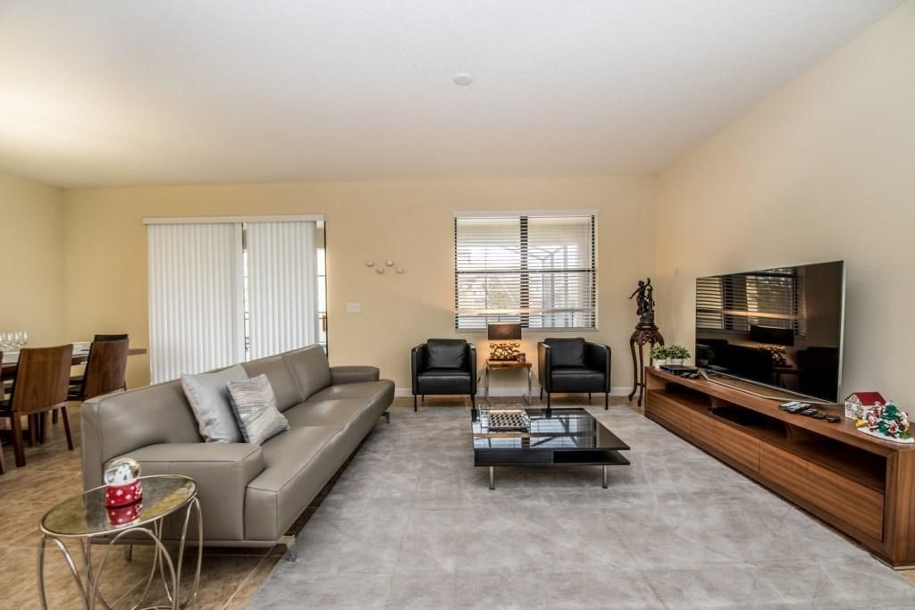 A modern living room with a sofa, two armchairs, a coffee table, a TV, and a dining area with chairs and a table.