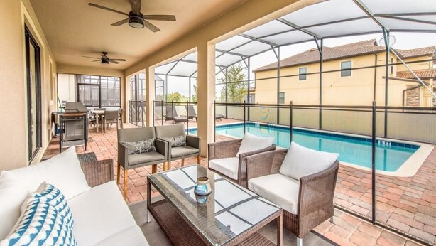 A covered patio area with outdoor furniture, a glass table, and a pool in the background.