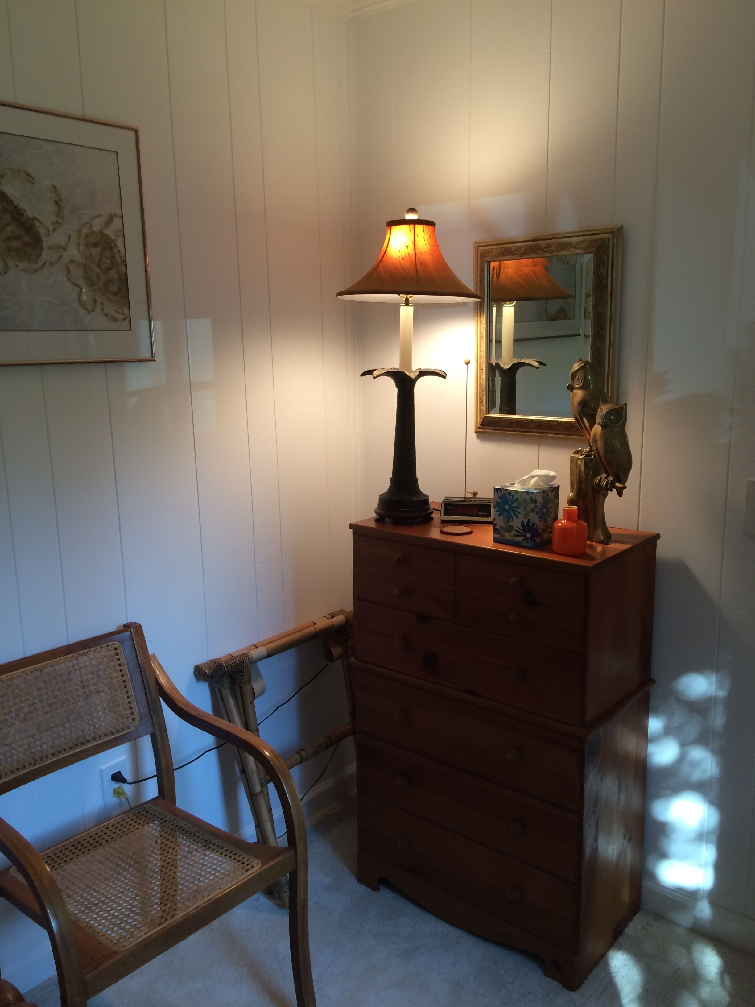 A room with a wooden dresser, a lamp, a chair, and a mirror on the wall.