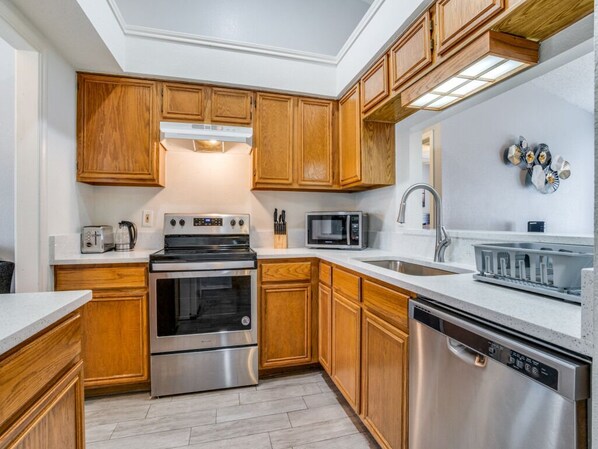 A modern kitchen with wooden cabinets, stainless steel appliances, and a white countertop.