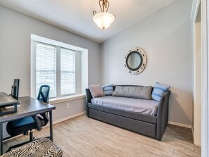 Habitación con sofá, una mesa y una silla. Se observa una ventana con persianas y un espejo montado en la pared.