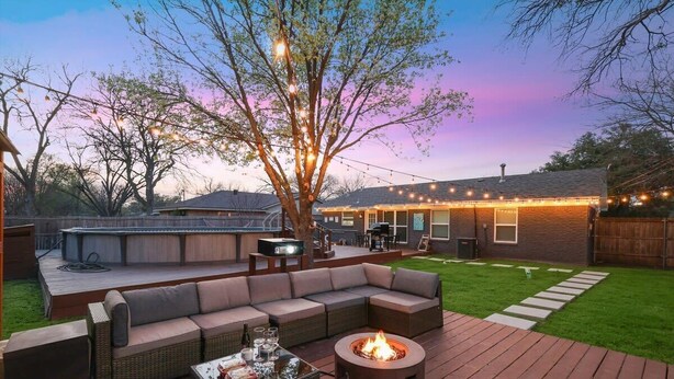 Ein Garten mit einer Holzterrasse, einem Feuerkorb, Gartenmöbeln und Lichterketten.