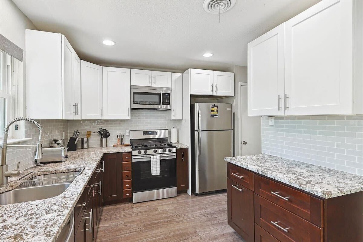 A modern kitchen with white cabinets, a stainless steel refrigerator, a built-in oven, and a microwave.