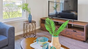 Ein Wohnzimmer mit Fernseher, einer Couch, einem Couchtisch mit Dekoration und einem Fenster mit Blick auf Bäume.