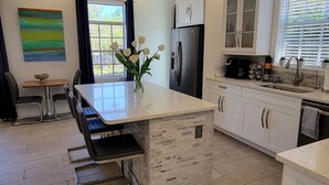 Een moderne keuken met een centraal eiland, witte kasten en een eethoek met tafel en stoelen.