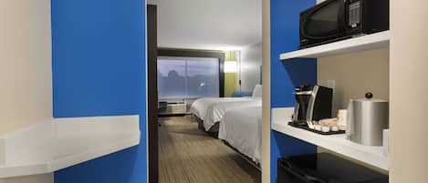 Habitación de hotel con cama, escritorio con microondas, cafetera y refrigerador pequeño.