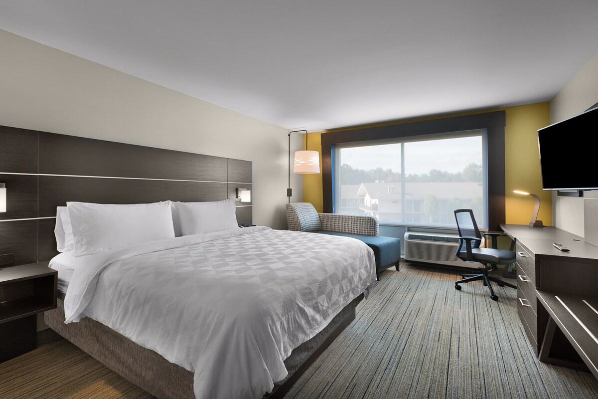 A hotel room with a large bed, a desk with a chair, a TV, and a window with a view.