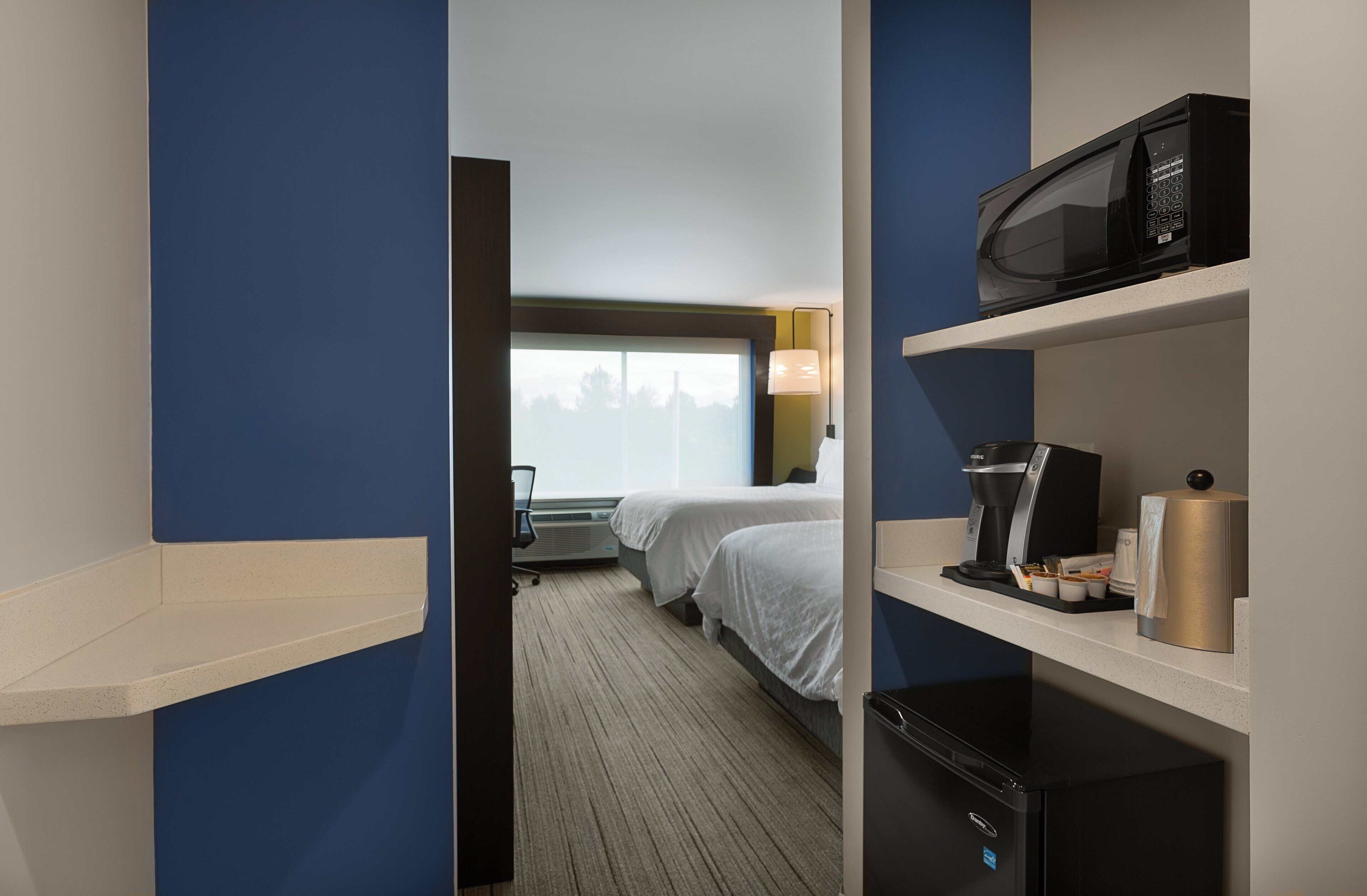 A hotel room with a bed, a microwave, a coffee maker, and a mini fridge.