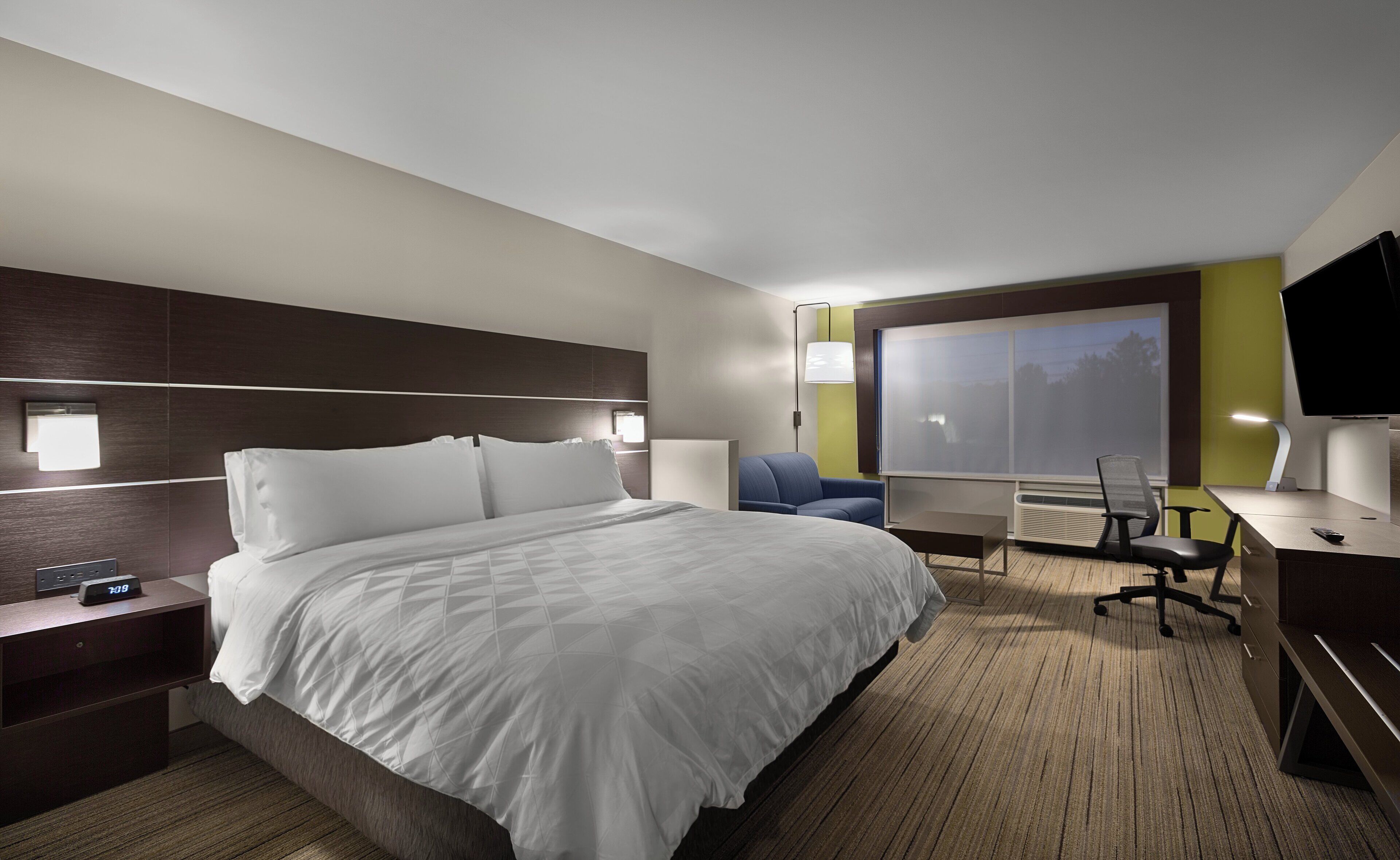 A hotel room with a large bed, a desk, a chair, a TV, and a window with a view.