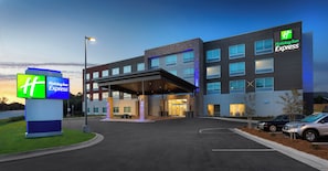 Un hotel Holiday Inn Express con un diseño moderno, que cuenta con un acceso cubierto y varios espacios de estacionamiento.