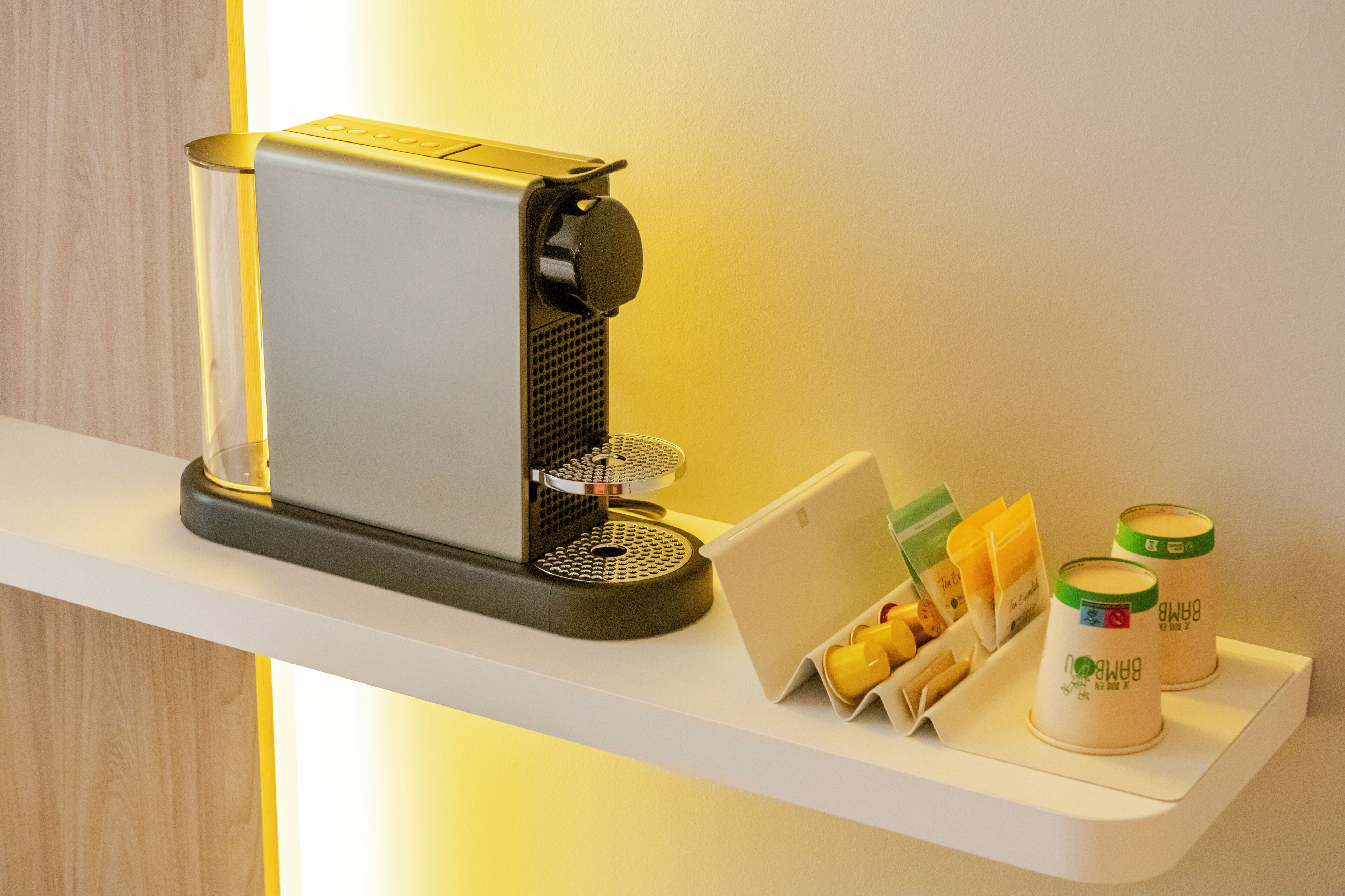 Une machine à café est posée sur une étagère blanche, avec un plateau contenant des tasses à café et une carte.