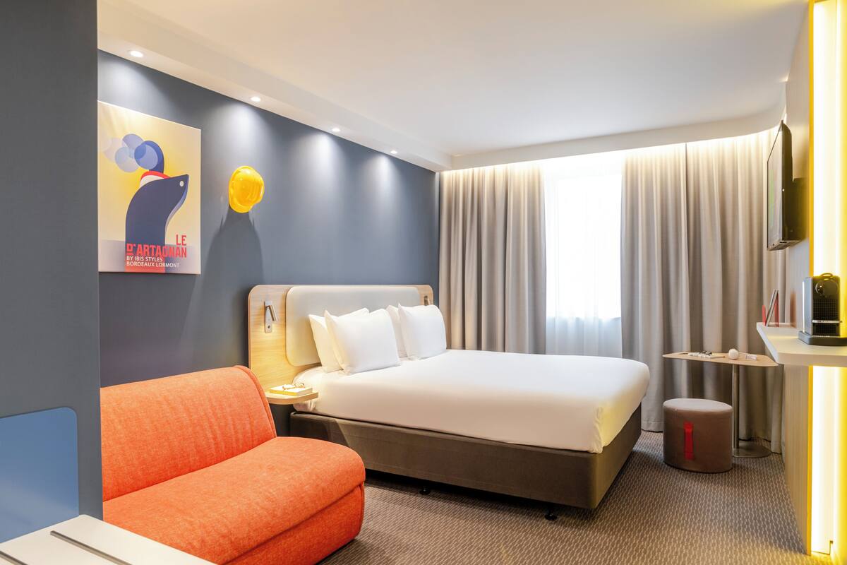 Une chambre d’hôtel avec un lit, un bureau, une chaise et un tableau au mur.