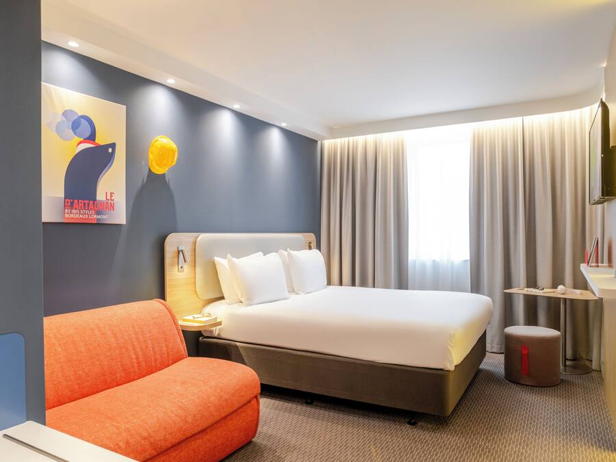 A hotel room with a bed, a desk, a chair, and a painting on the wall.