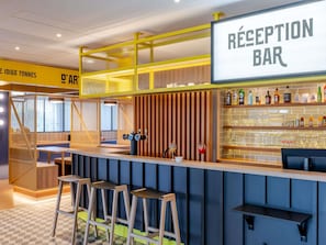 A reception bar with a sign, bar stools, a counter, and shelves with bottles and glasses. - ibis Styles Bordeaux Lormont (Lormont)