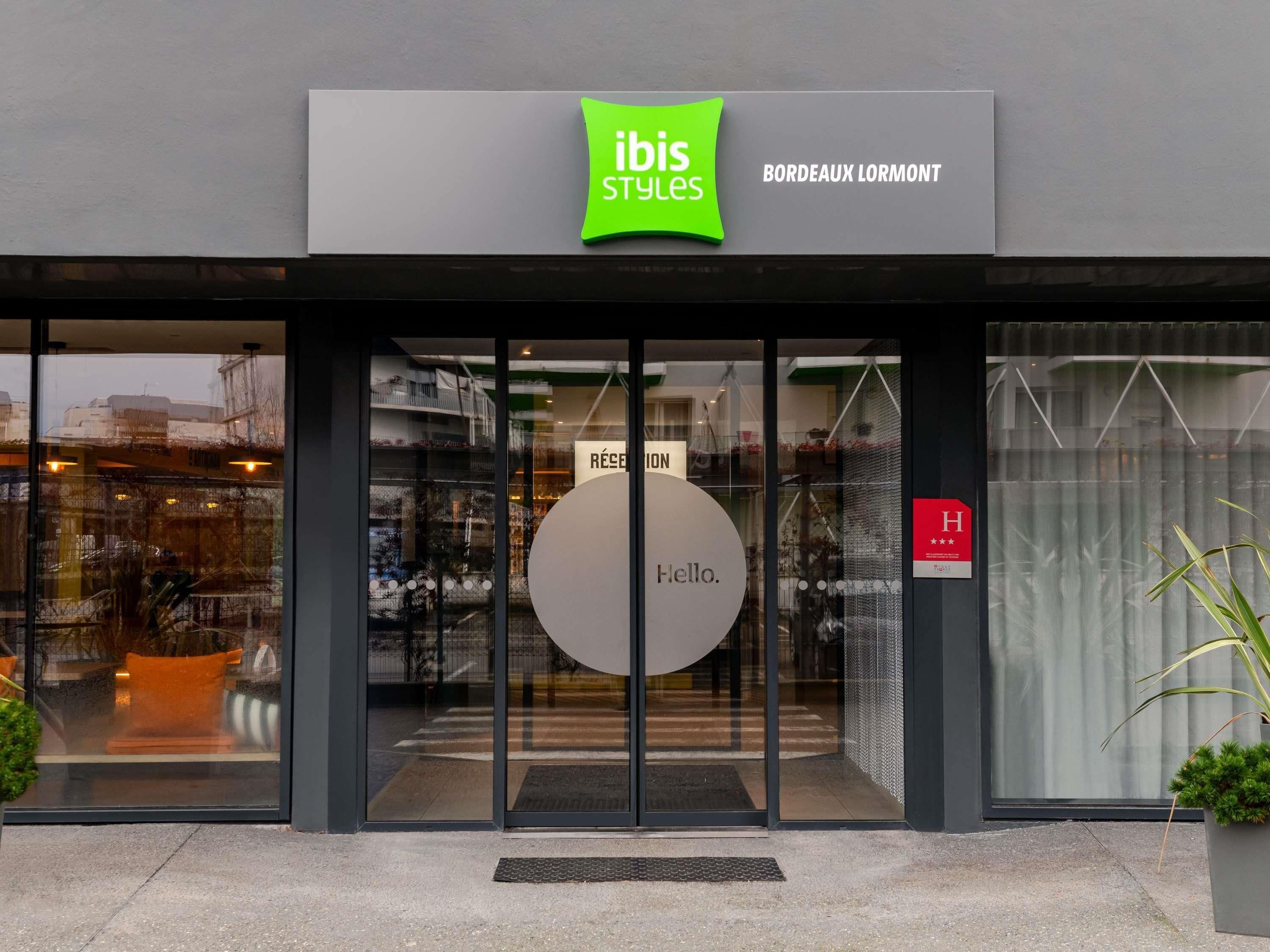 Une devanture avec une porte d’entrée en verre, une enseigne indiquant « ibis Styles » et un panneau « bonjour » sur la porte.