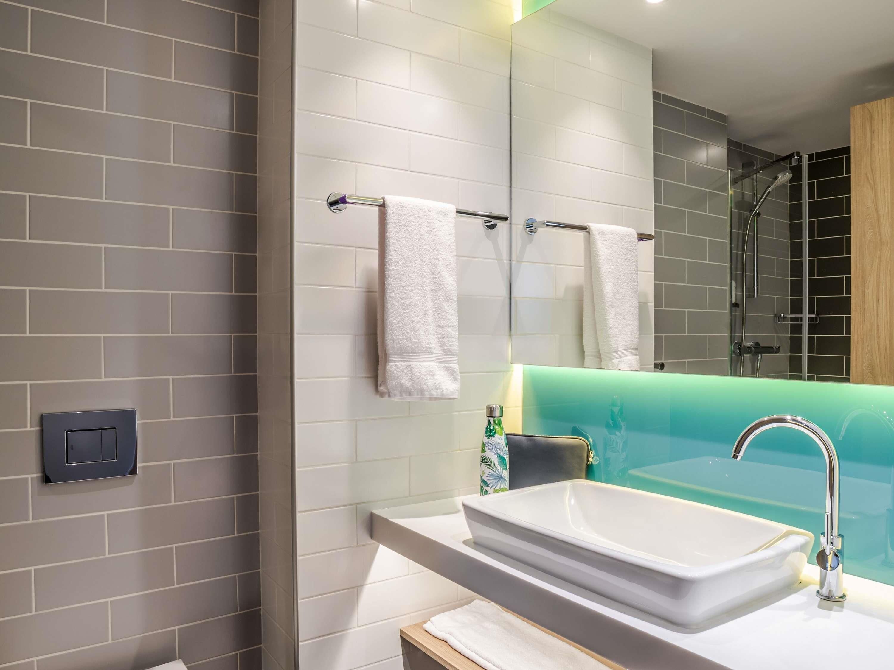 A modern bathroom with a large mirror, a white sink, and a shower area.