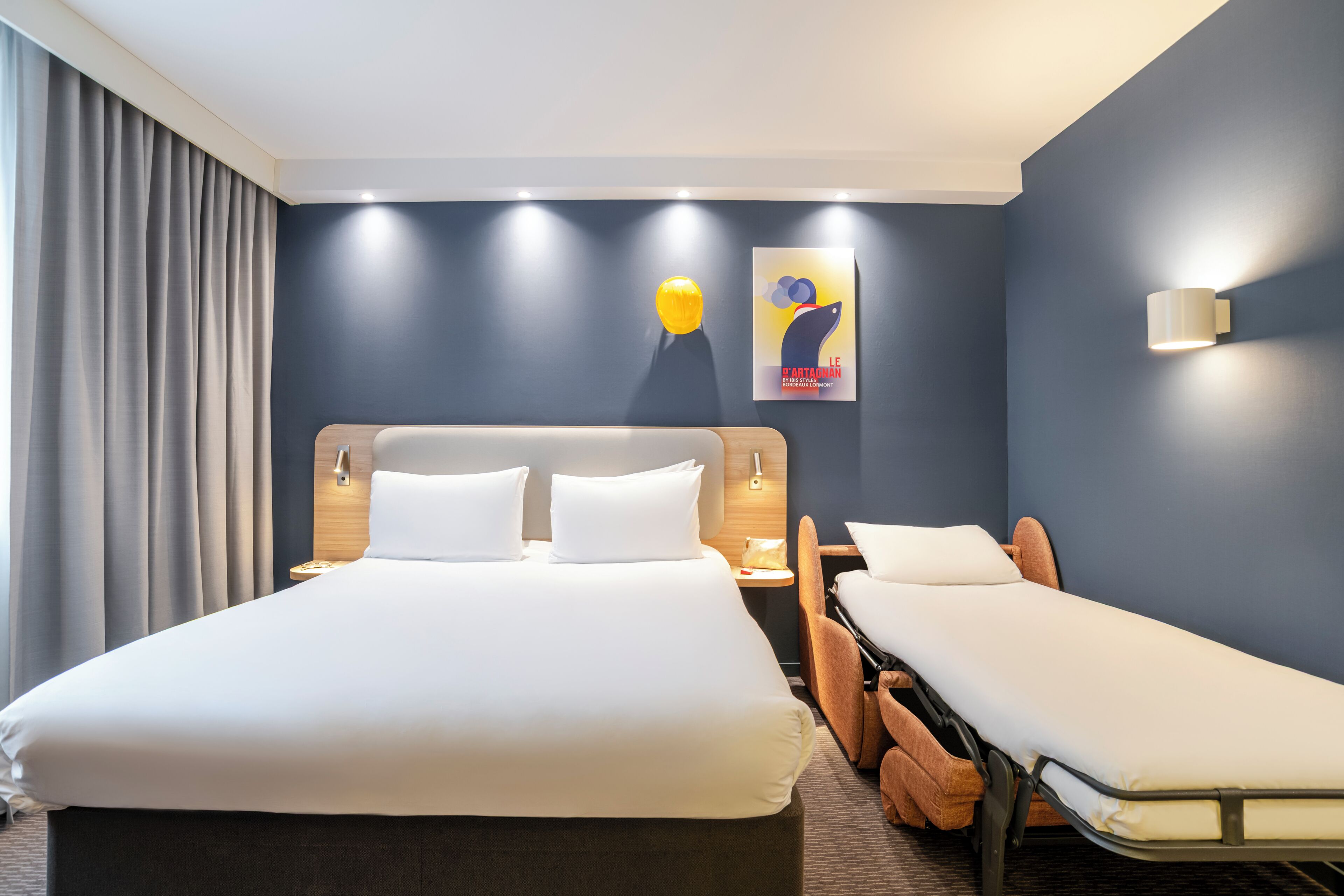 Een hotelkamer met een groot bed, een kleiner bed, een bureau en een stoel.