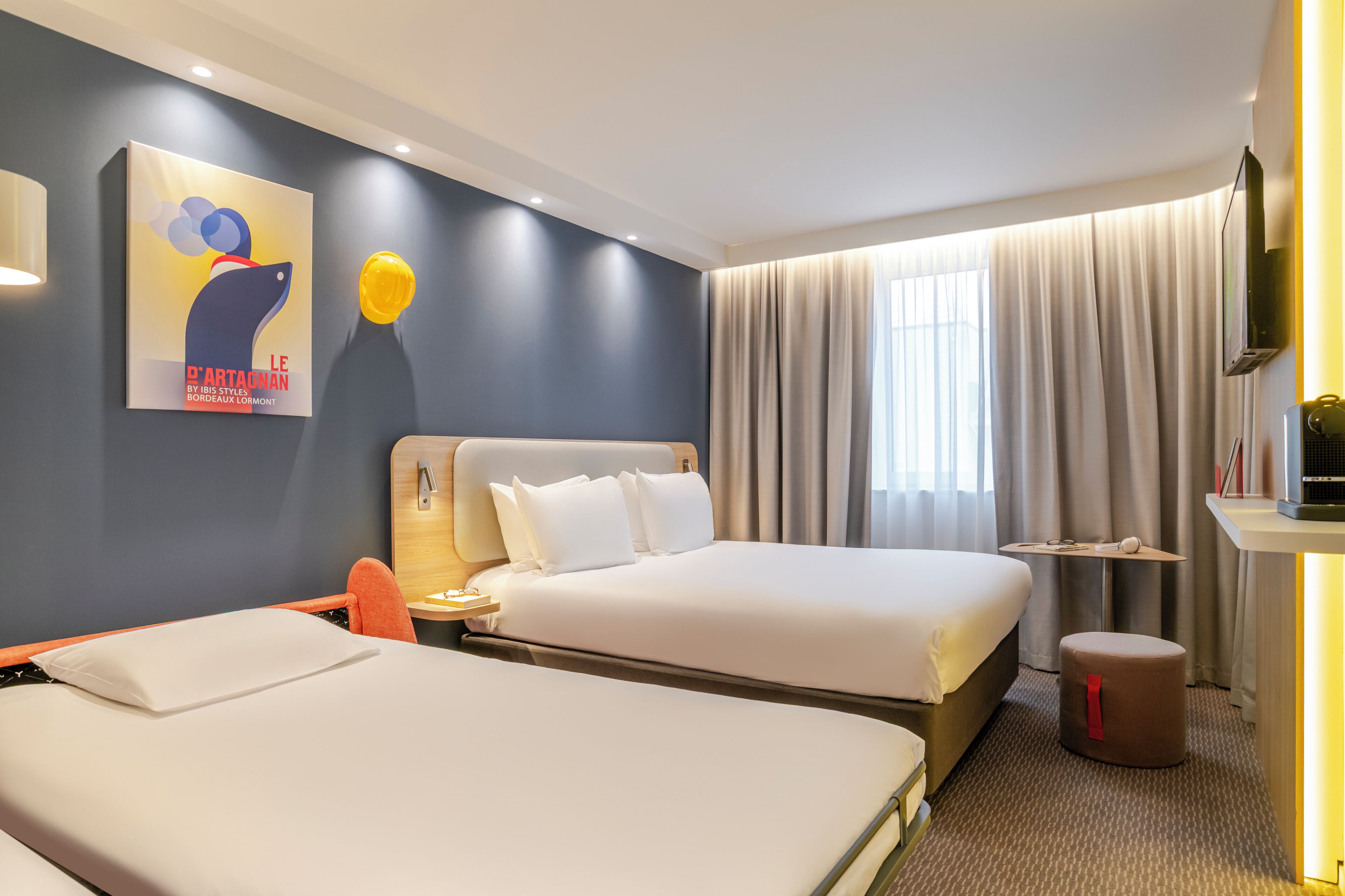Een hotelkamer met twee bedden, een kleine tafel, een televisie en een schilderij aan de muur.