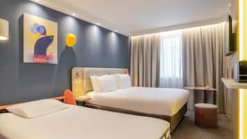 Een hotelkamer met twee bedden, een kleine tafel, een televisie en een schilderij aan de muur.