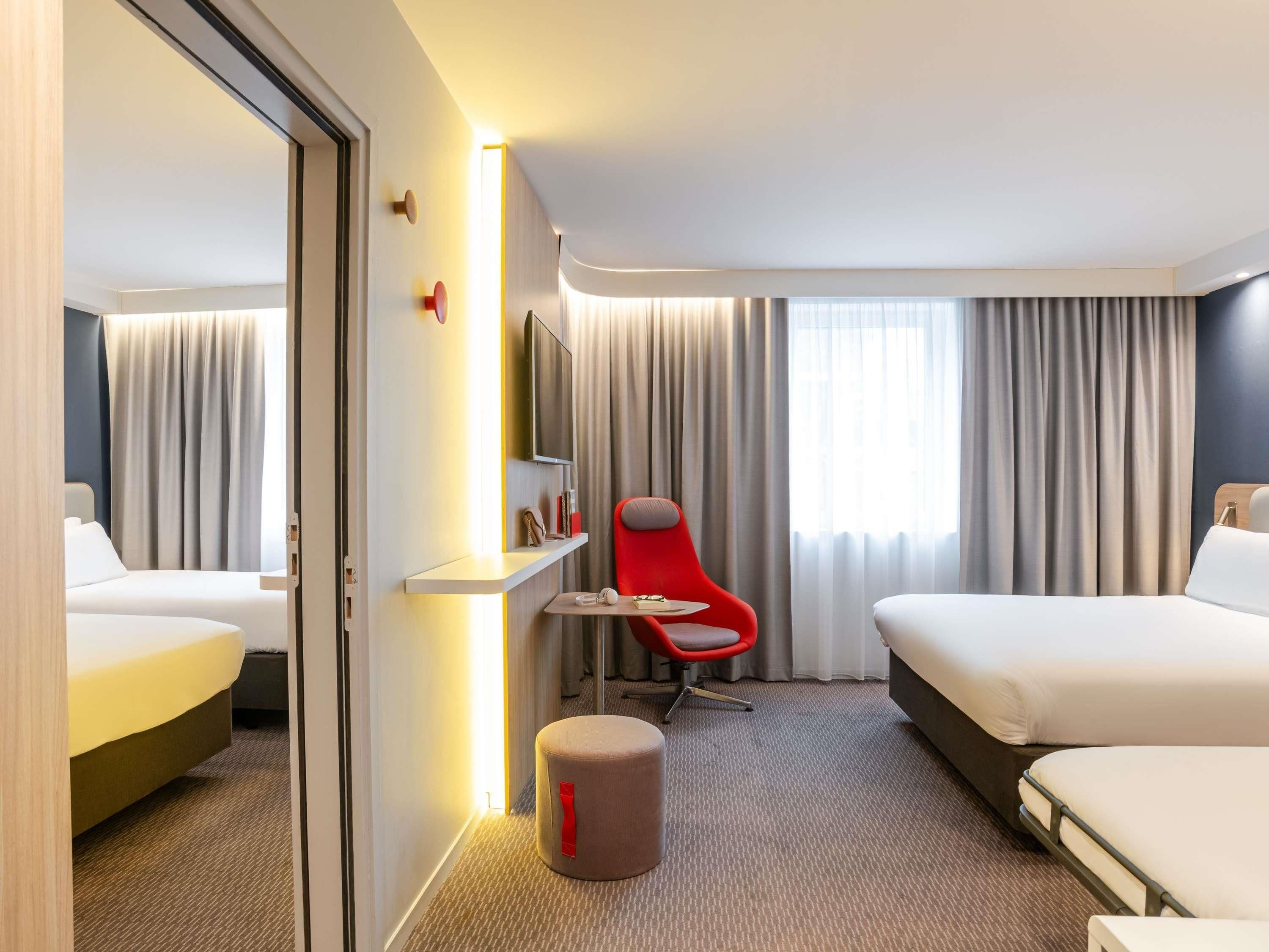 Een hotelkamer met twee bedden, een rode stoel, een klein tafeltje, een spiegel en een televisie.