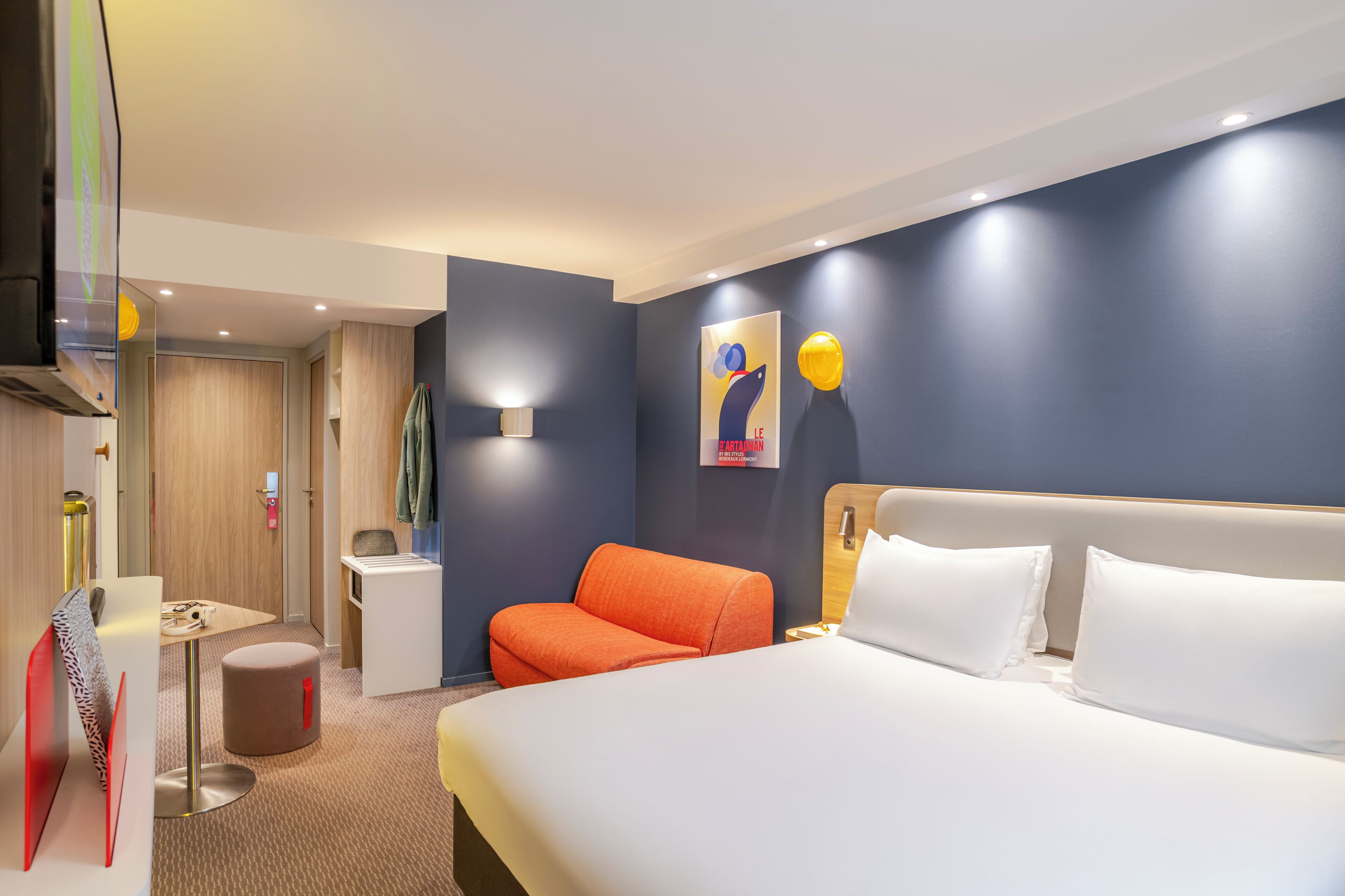 Una habitación de hotel moderna con una cama grande, un área de descanso con una silla, una mesita y un televisor montado en la pared.
