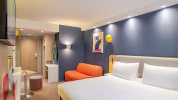 Una habitación de hotel moderna con una cama grande, un área de descanso con una silla, una mesita y un televisor montado en la pared.