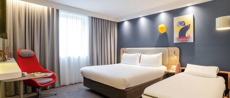 Habitación de hotel con una cama grande, otra más pequeña, un escritorio con una silla y una ventana con cortinas.