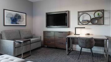 A modern living room with a sofa, a desk, a TV, and a framed artwork on the wall.
