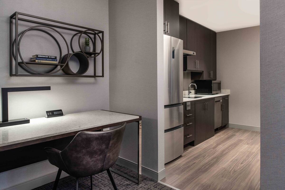 A modern kitchen with dark cabinets, stainless steel appliances, and a marble countertop.