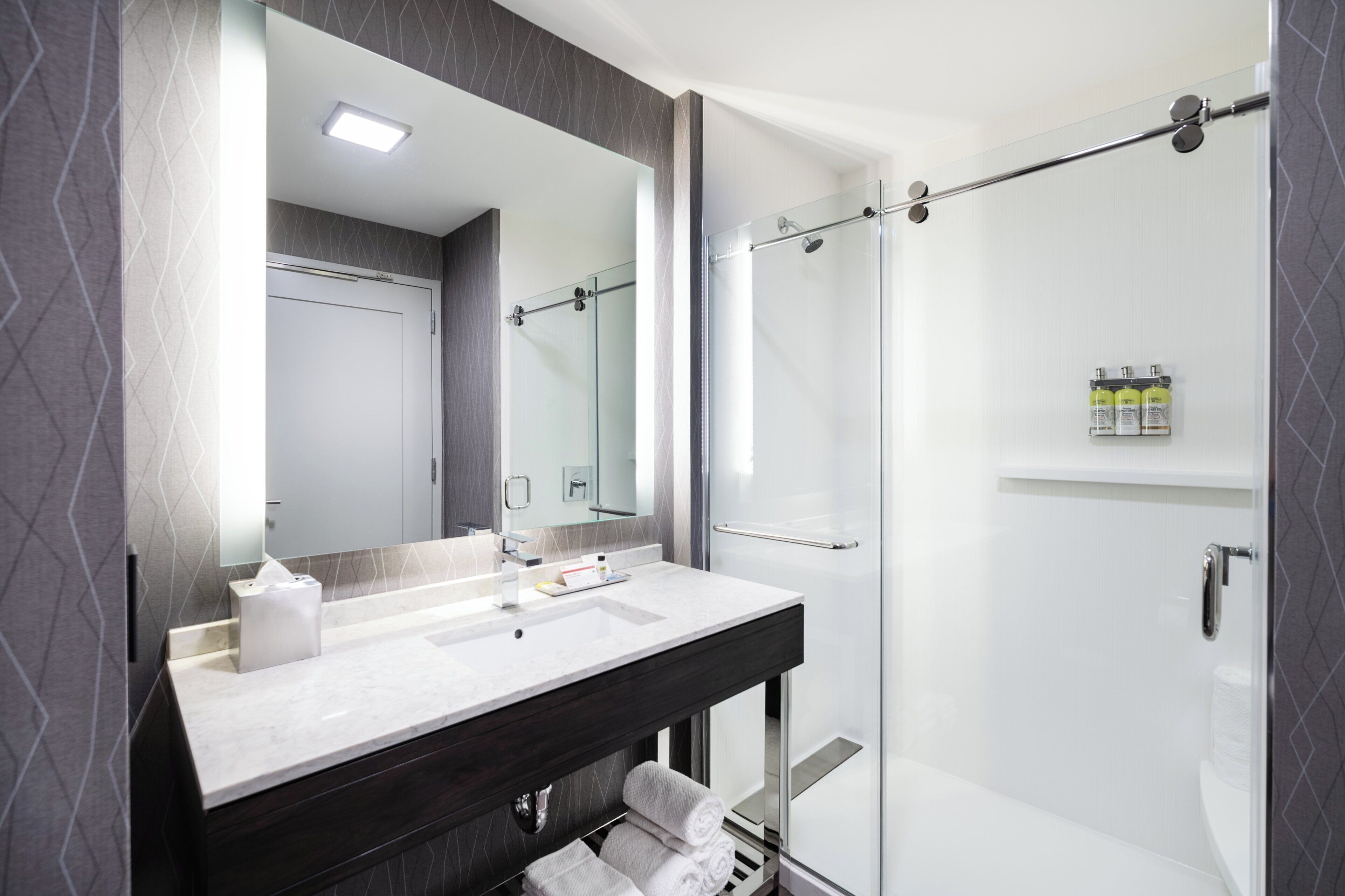 A modern bathroom with a glass shower enclosure, a vanity with a mirror, and a towel rack.