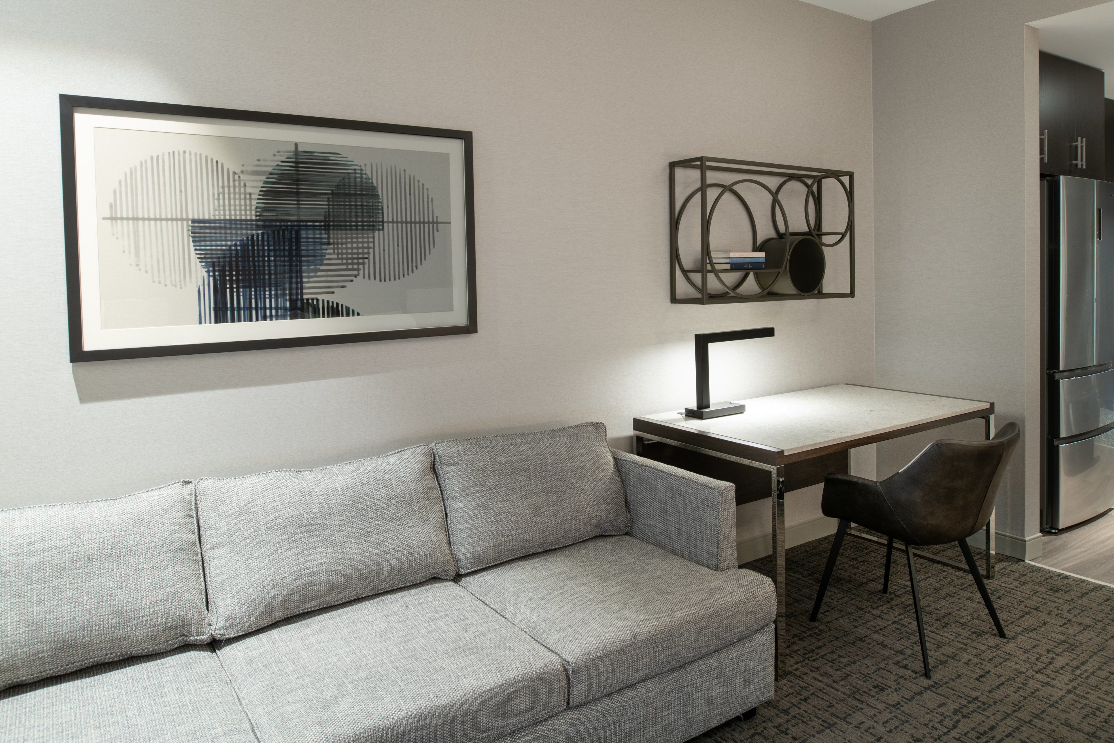 A modern living room with a grey sofa, a desk, and a chair. There are framed artworks on the wall.
