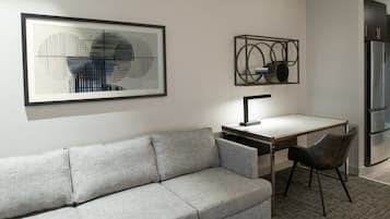 Una sala moderna con un sofá gris, un escritorio y una silla. Hay obras de arte enmarcadas en la pared.