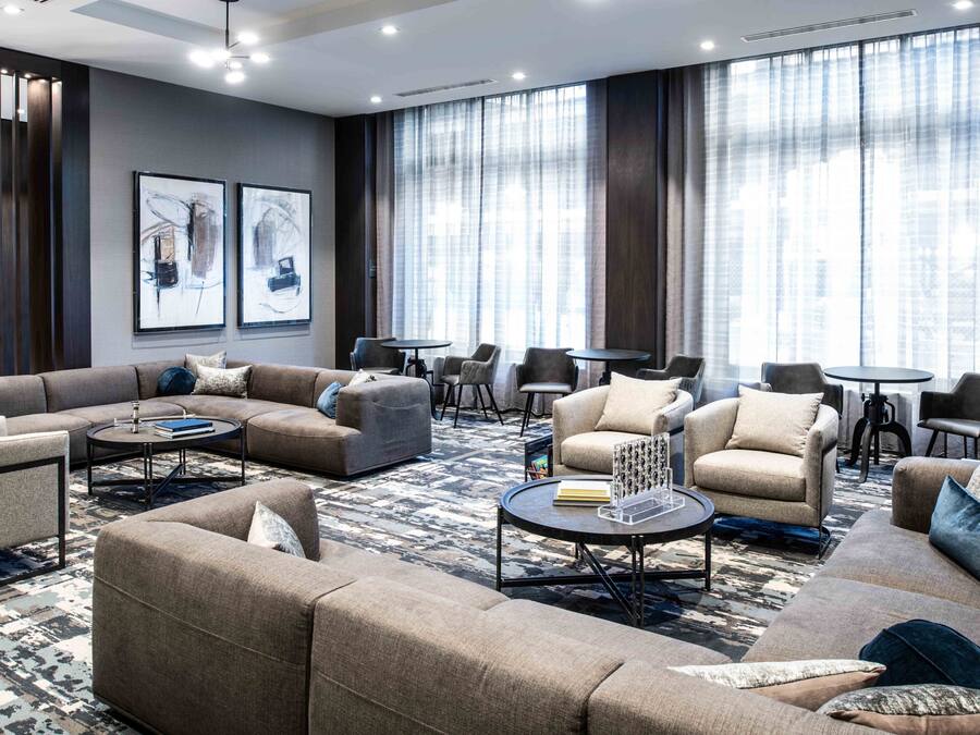 Une chambre d’hôtel moderne comprenant un canapé d’angle, des fauteuils, une table basse et un coin repas avec une petite table et des chaises.