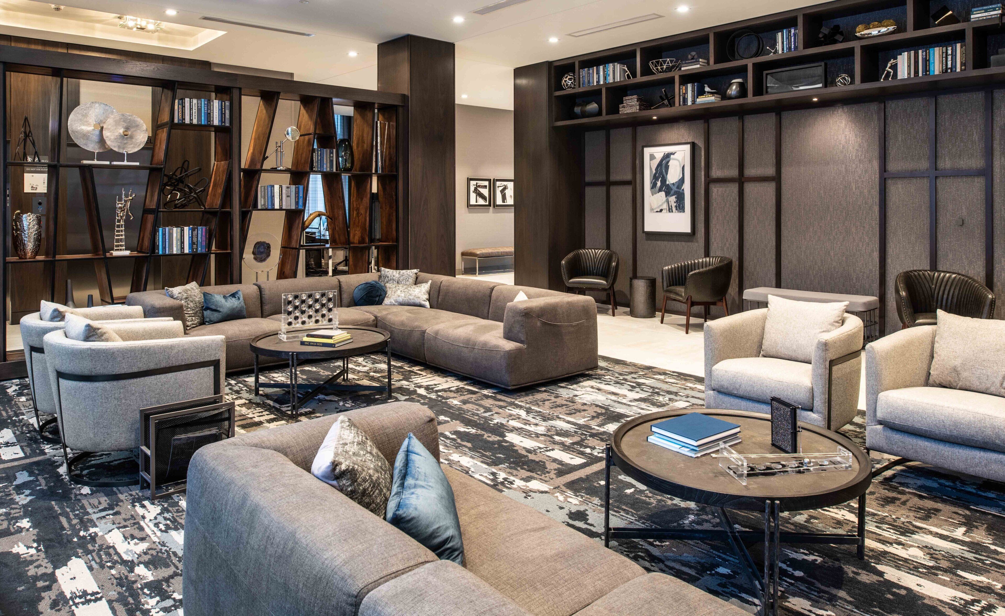 Una sala de estar moderna con un sofá modular, sillones, una mesa de centro y una estantería llena de libros y objetos decorativos.