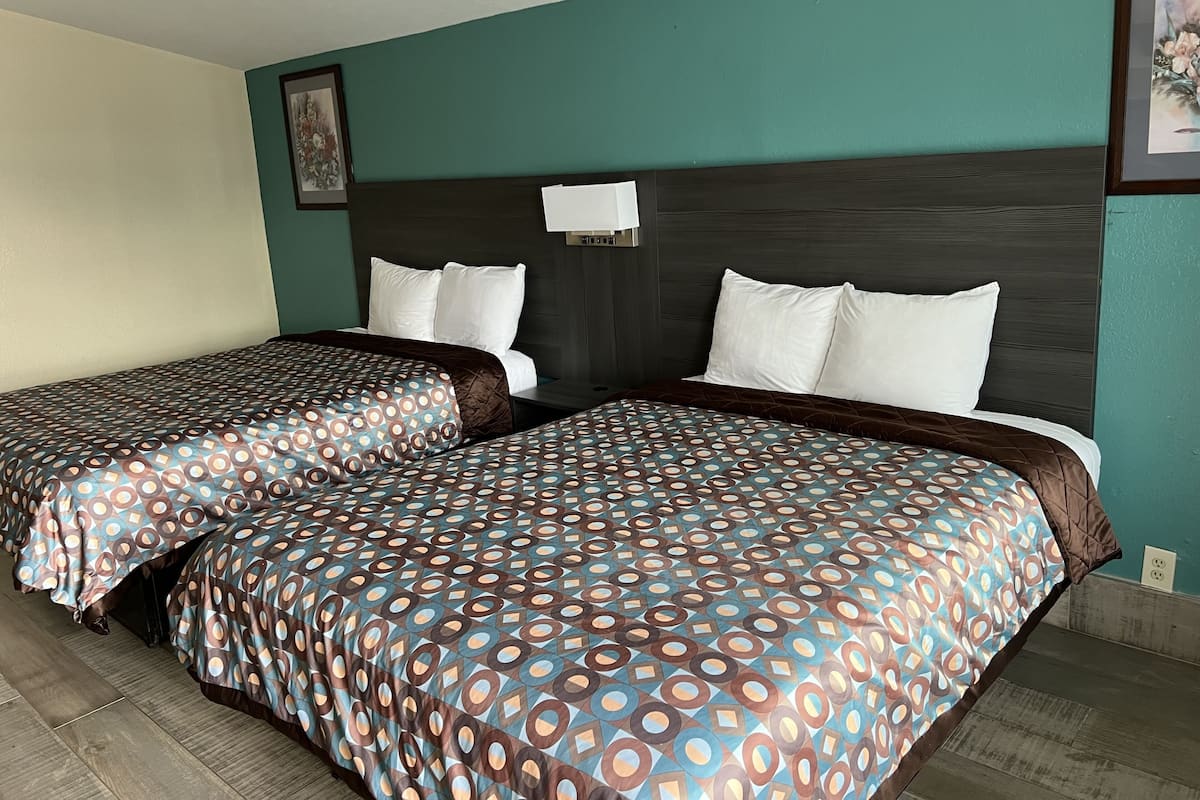 A hotel room with two beds, teal walls, and a dark wood headboard.