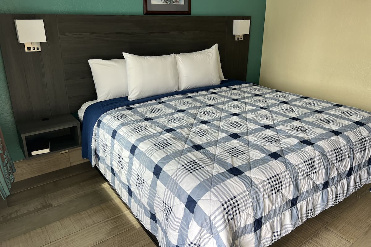 A neatly made bed with a checkered bedspread, a wooden nightstand with a drawer, and a wall-mounted light fixture.