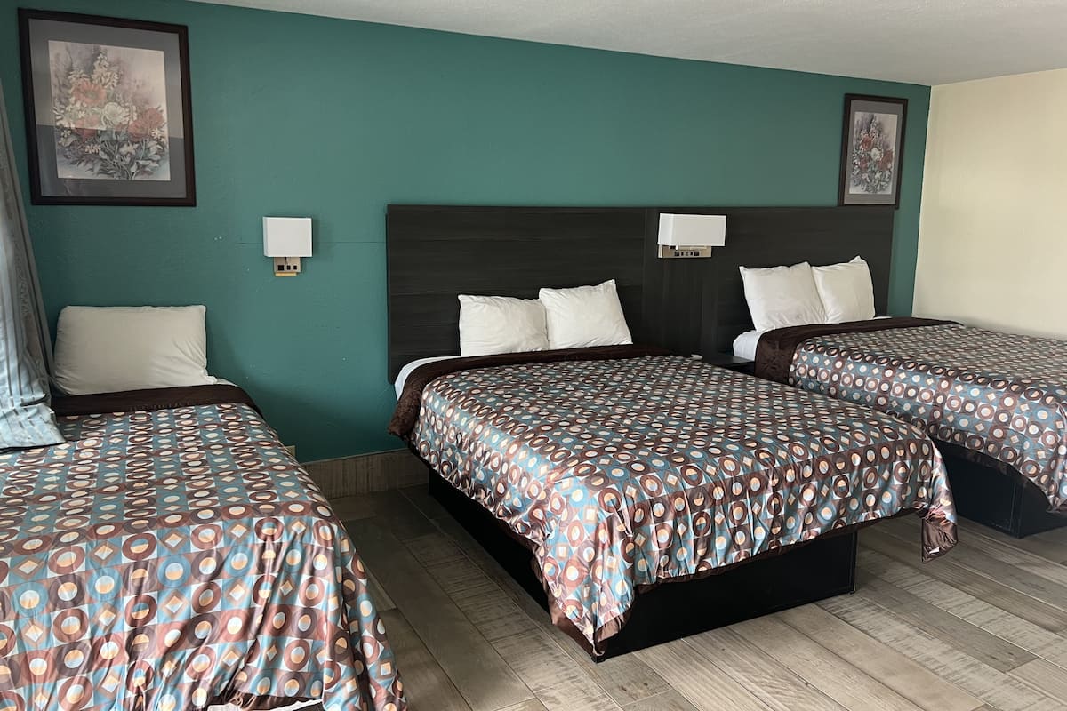A hotel room with three beds, teal walls, and a dark headboard.