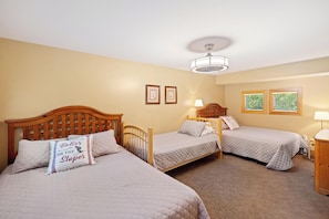 A hotel room with two single beds, a wooden headboard, a bedside table with a lamp, and a ceiling light fixture. - Ski in/out condo on Disciples Ridge- Four bedroom Condo (Boyne Falls)