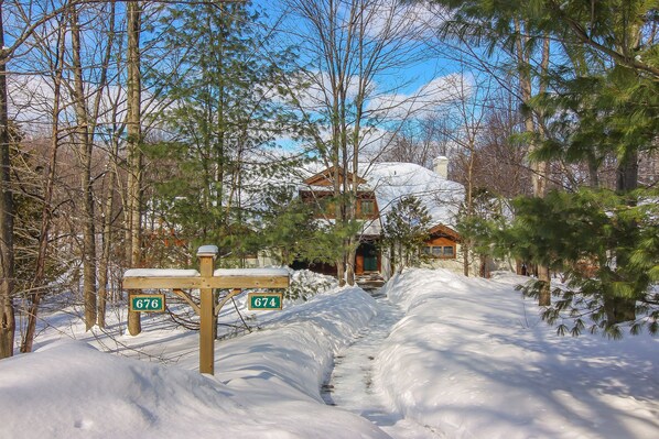 A snow-covered path leading to a house with a wooden bench and two signs indicating numbers 674 and 676. - Ski in/out condo on Disciples Ridge- Four bedroom Condo (Boyne Falls)