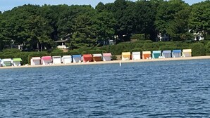 Udsigt over vandet med farverige strandhuse og en skovklædt bakke i baggrunden.