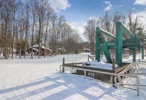A snow-covered outdoor area with a wooden structure and metal railings, surrounded by leafless trees and a clear sky. - Ski in/out condo on Disciples Ridge- Four bedroom Condo (Boyne Falls)