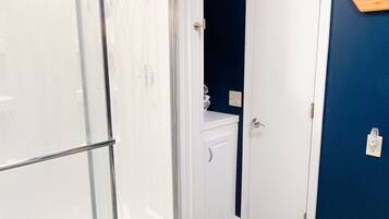 A bathroom with a glass shower door, a white cabinet, a blue wall, and a patterned rug.