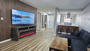 A modern living room with a flat-screen TV, wooden flooring, a dark sofa, and a wooden coffee table. - Olympic Suites Inn (Forks)