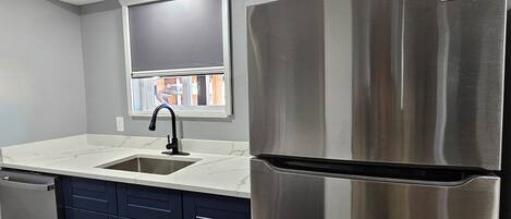 A modern kitchen with a stainless steel refrigerator, a sink, and dark blue cabinets.