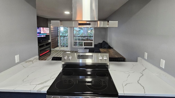 A modern kitchen with a central island, stainless steel appliances, and a large window overlooking a balcony. - Olympic Suites Inn (Forks)