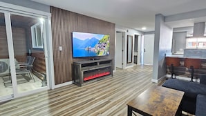 A modern living room with a flat-screen TV, wooden flooring, a sofa, and a kitchen area with a bar. - Olympic Suites Inn (Forks)