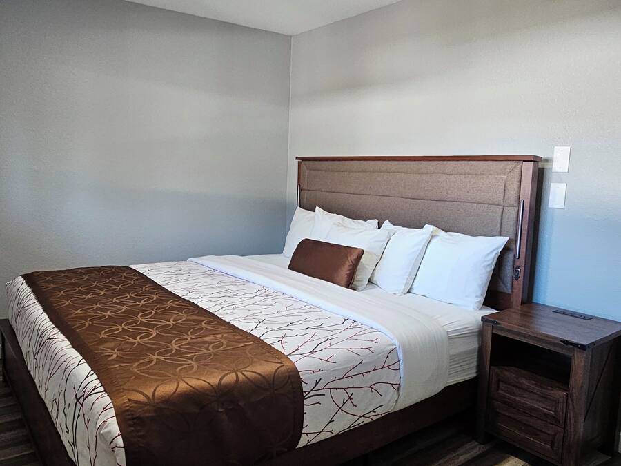 A hotel room with a wooden bed, white bedding, and a brown accent throw.